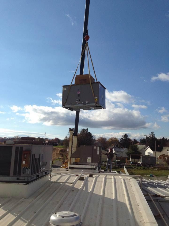 Crane lifting HVAC unit onto a rooftop on a sunny day.