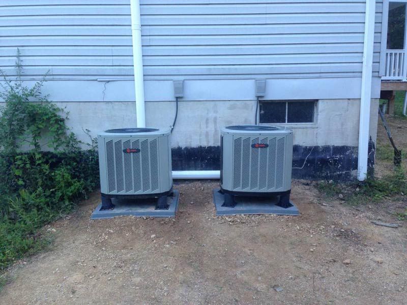 Two gray air conditioning units on concrete pads next to a building with gray siding.
