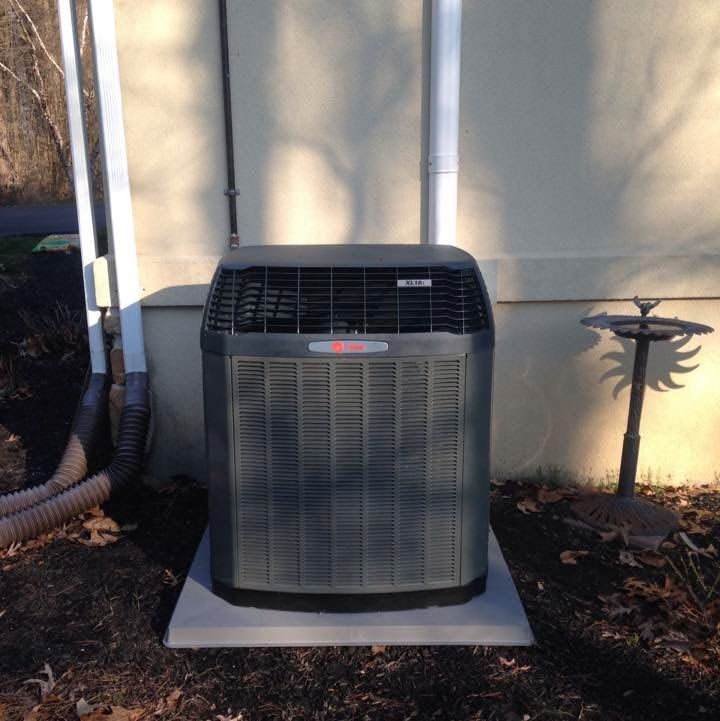 Gray air conditioning unit on a concrete pad, next to a building wall.