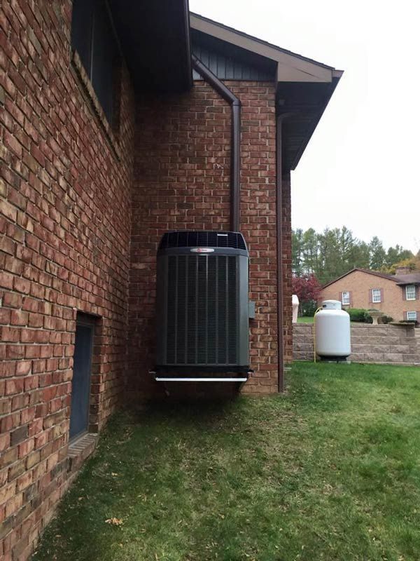 HVAC unit attached to a brick building. Black metal, outdoors on grass. Propane tank visible.