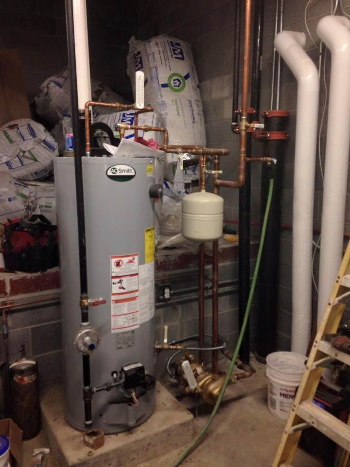 A water heater with copper pipes, expansion tank, and white insulation. A bucket and ladder are nearby.