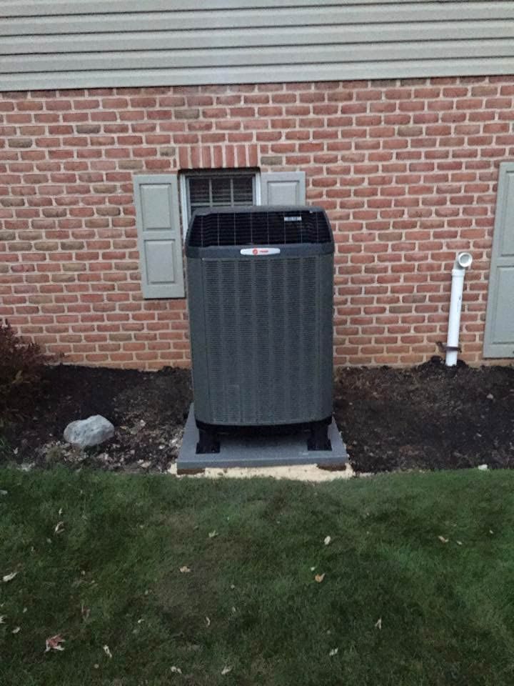 Outdoor air conditioning unit against a brick wall with window and shutters.