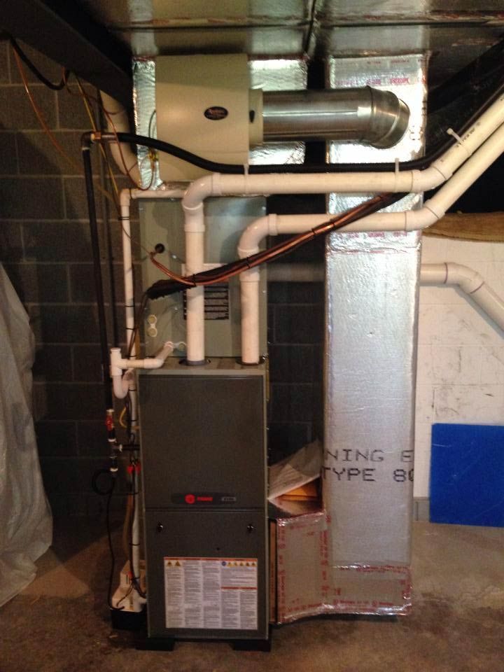 Furnace and humidifier unit in a basement setting. Gray metal with white pipes, silver ductwork, and black brick wall.