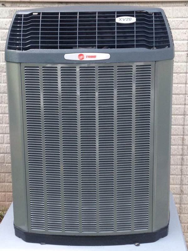 Gray Trane air conditioner unit outdoors, against a brick wall.