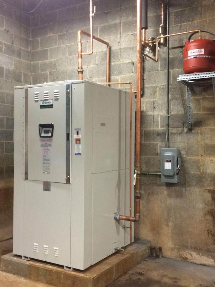 Large beige HVAC unit in a concrete basement with copper pipes and a red expansion tank.