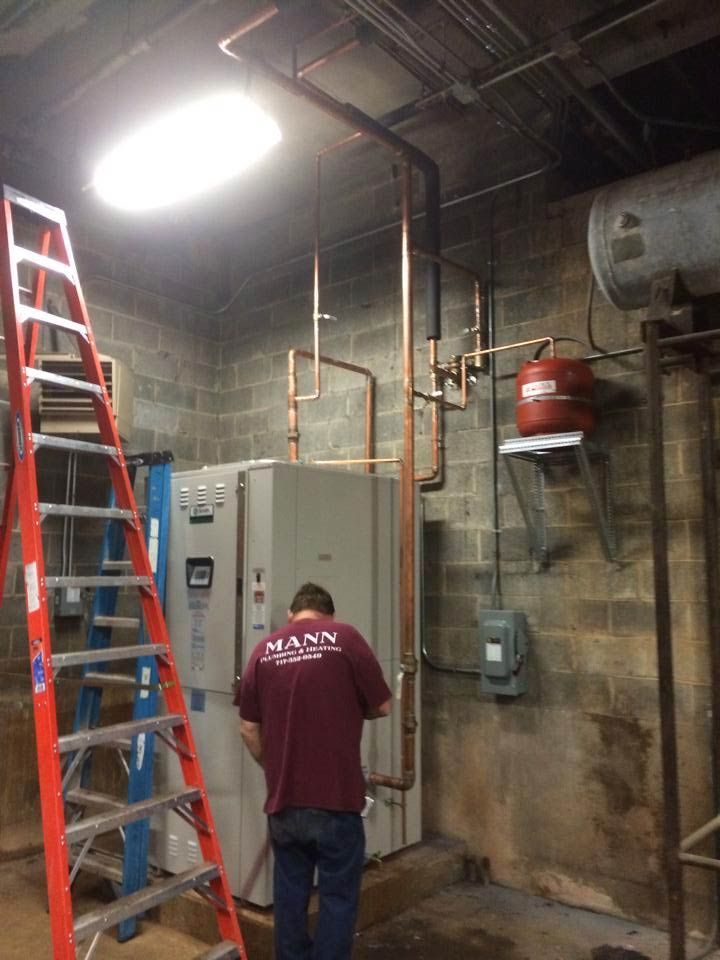 Plumber working on copper pipes in a utility room with a water heater and ladder.