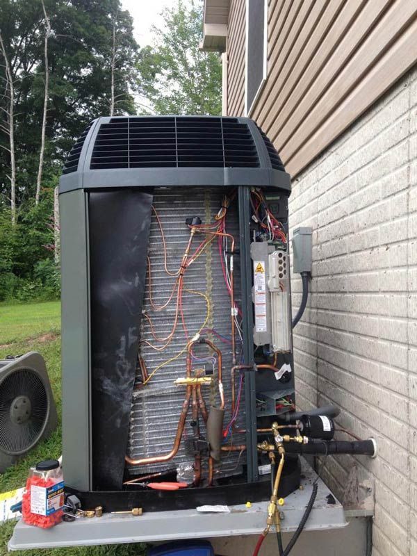 An air conditioning unit being serviced outdoors, with exposed internal components and tools.