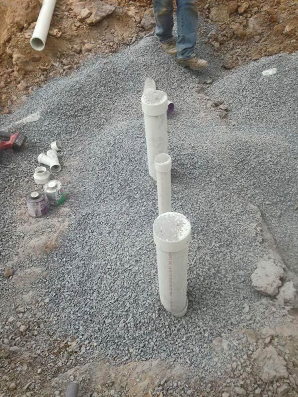 Plumbing pipes installed in gravel bed, a person in blue jeans stands nearby.