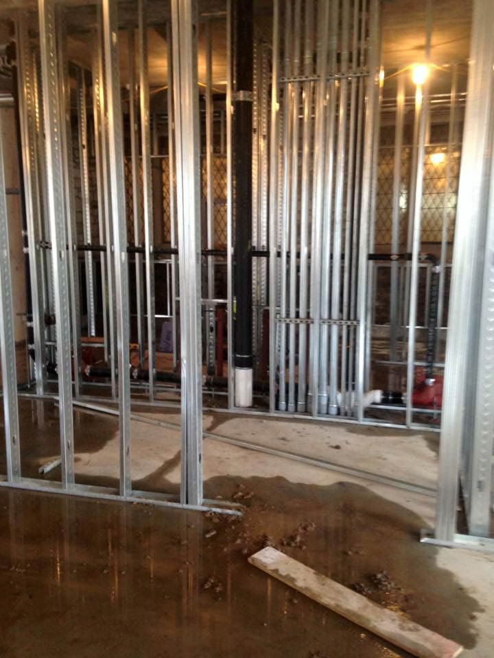 Metal framing and pipes inside a room under construction with a wet floor.