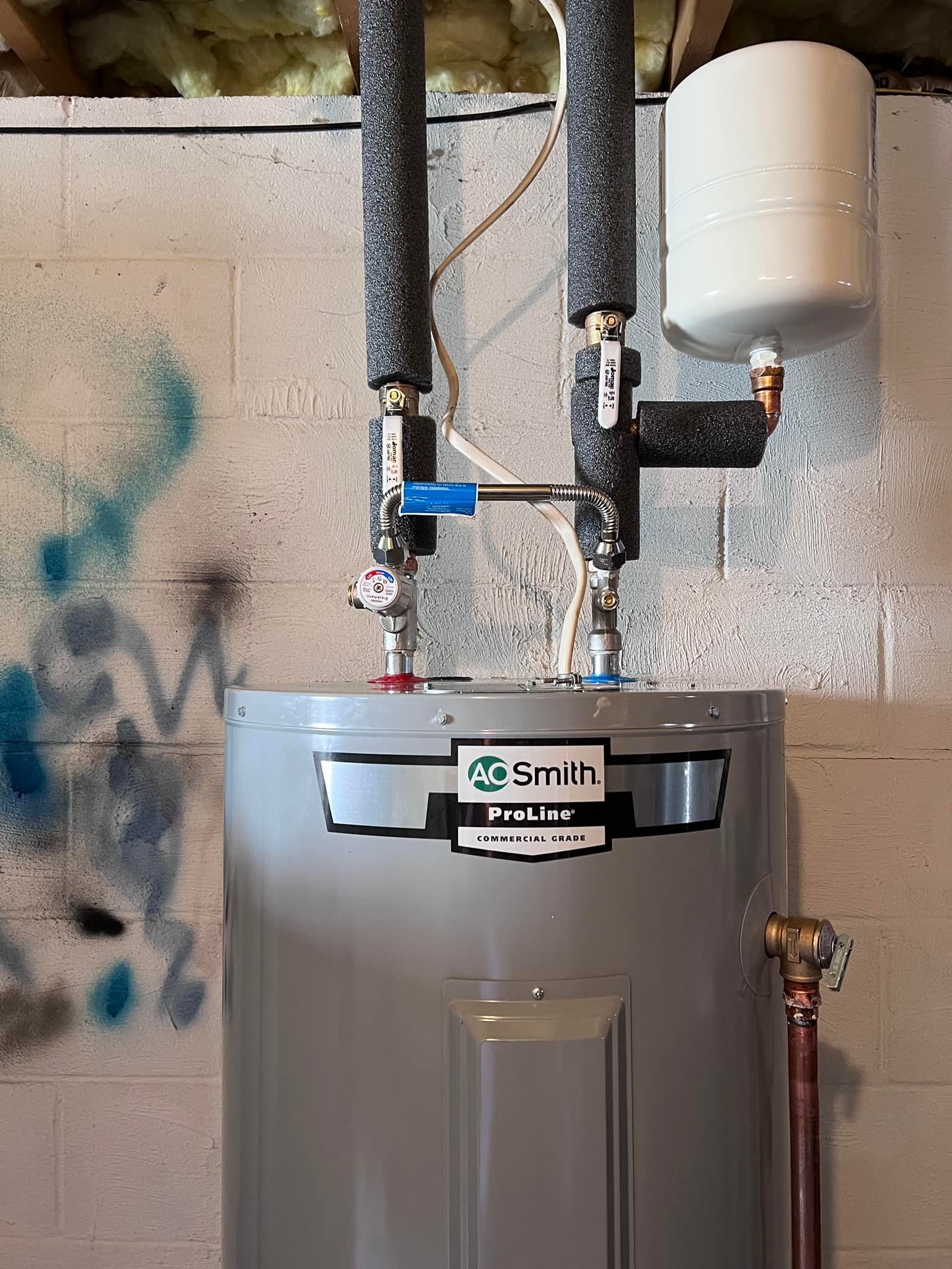 A water heater with pipes and an expansion tank in a basement setting.