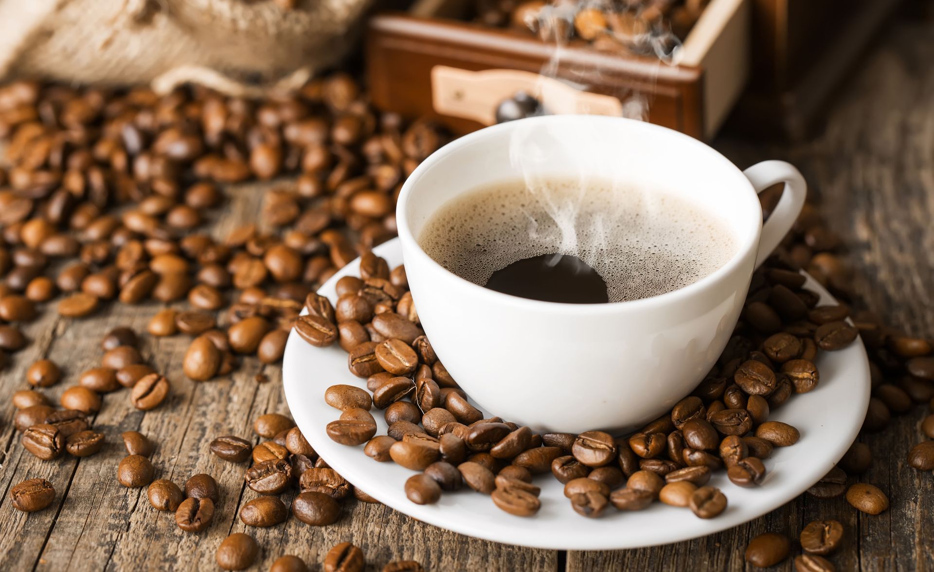 White cup of latte on a saucer with latte art, sitting on a wooden surface, with a spoon.