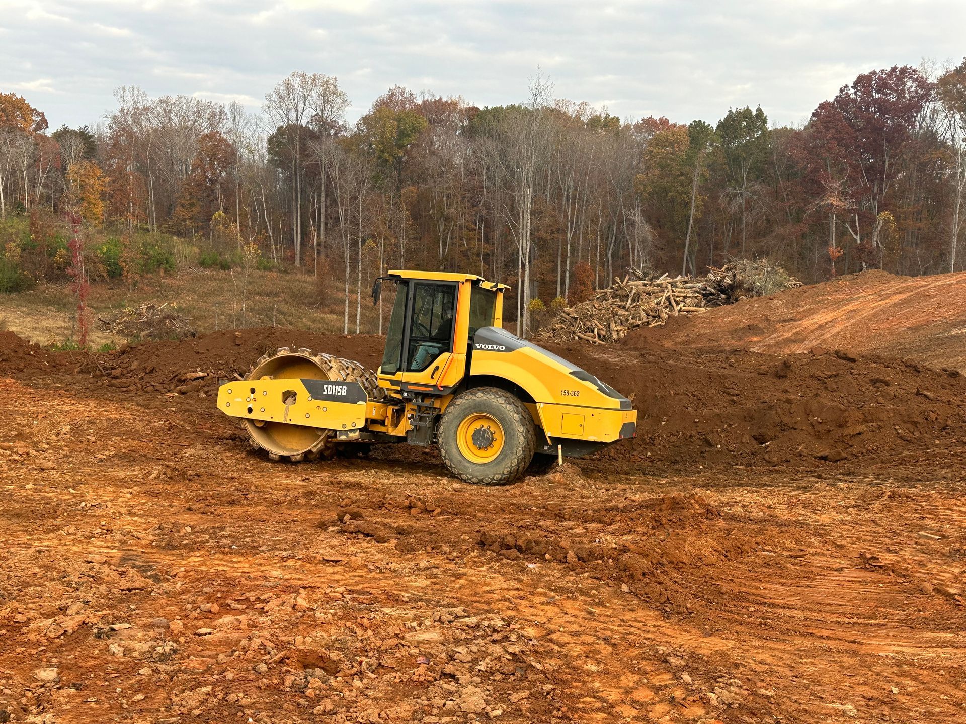 Yellow construction roller on a dirt site with autumn trees in the background