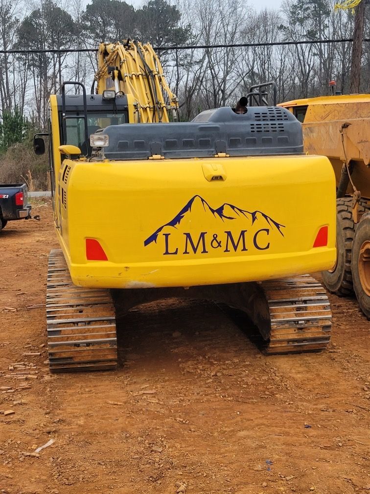 Yellow excavator on muddy ground with LM&MC logo, viewed from the rear