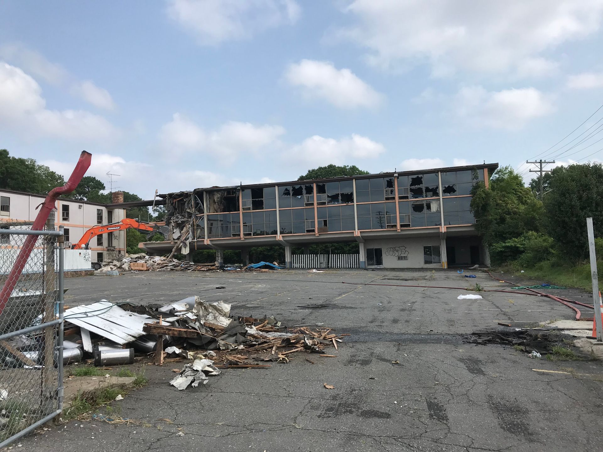 Demolished building site with rubble and a partially standing structure behind a chain-link fence