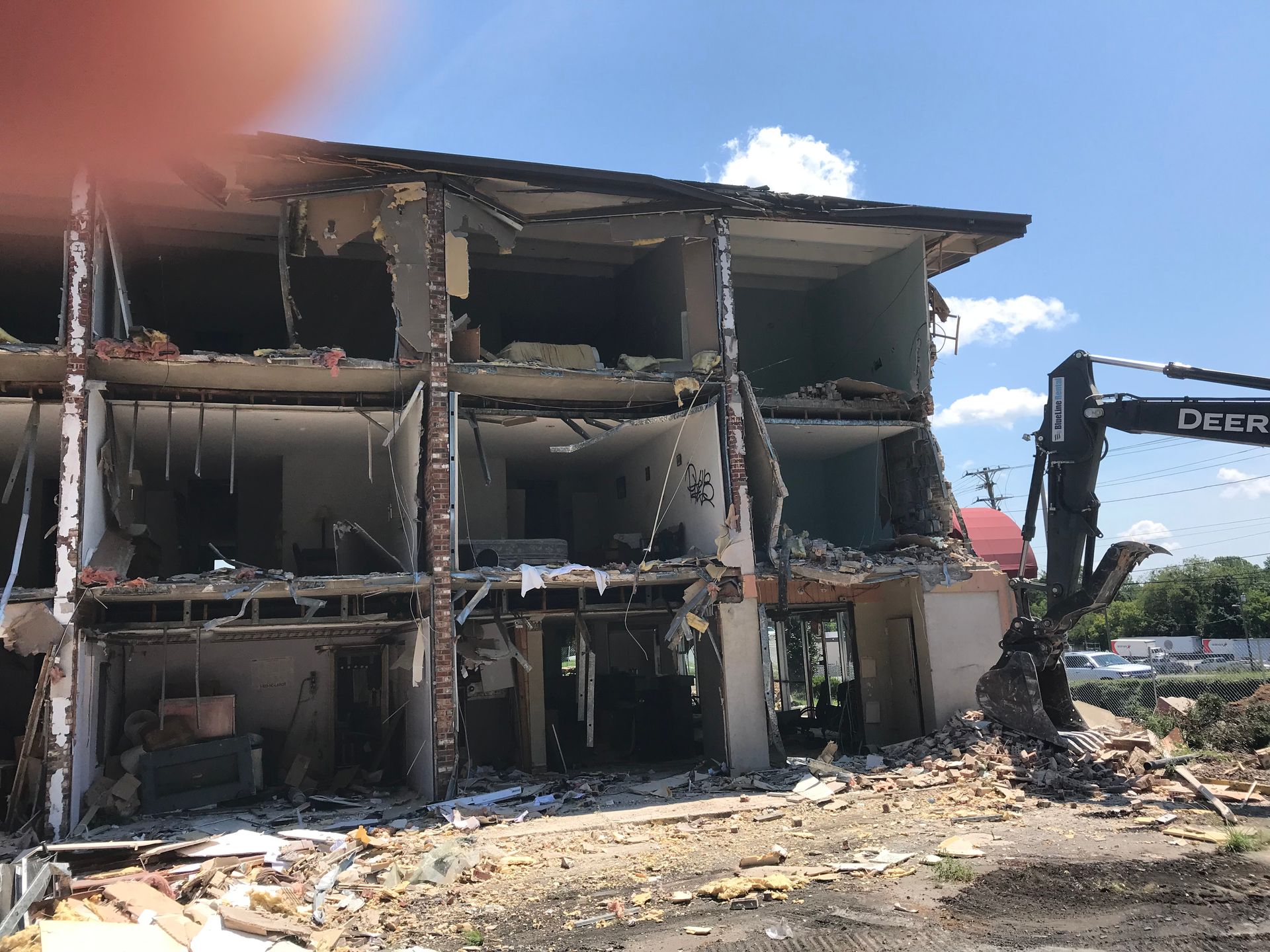 Partially demolished building with rubble and an excavator beside it under a clear sky