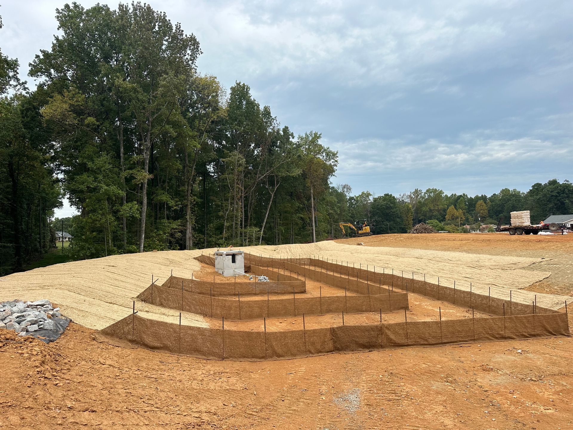 Terraced dirt foundation at a construction site with trees and cloudy sky in the background