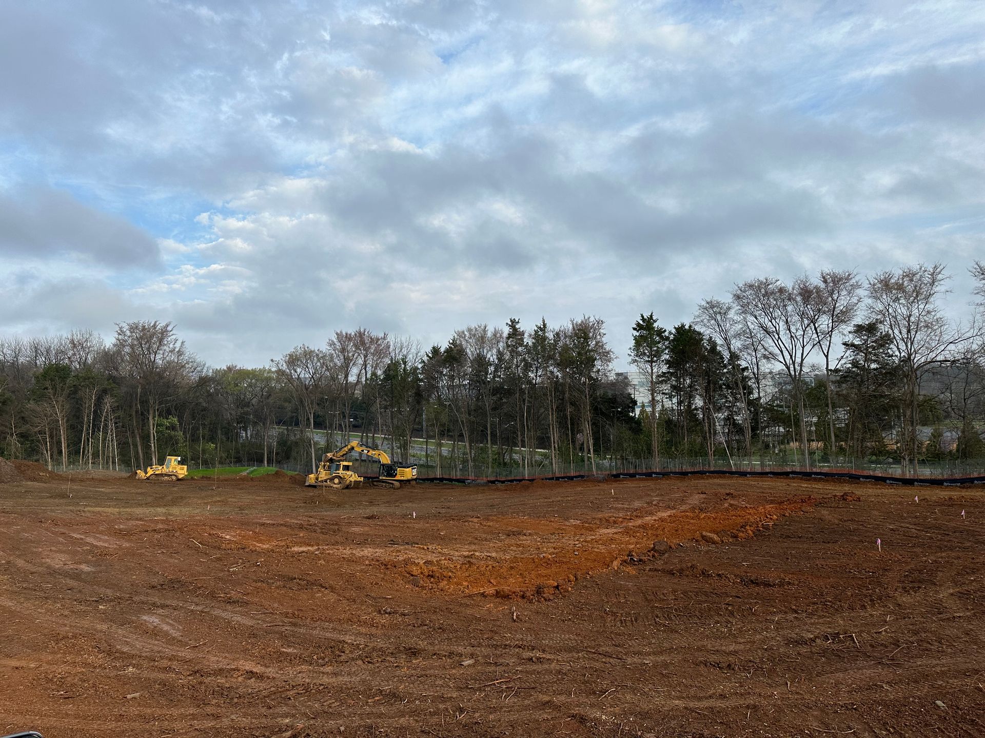 Construction site with yellow excavators on a bare dirt field under a cloudy sky