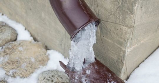 Frozen downspout draining ice onto snow beside a building wall