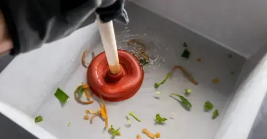 Hand using a white stick to stir a red dough ring on a tray with scattered vegetable bits