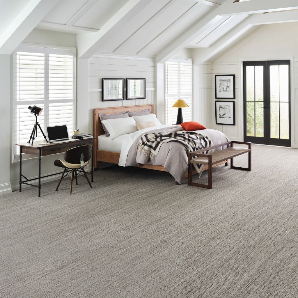 Bedroom with a bed, desk, windows, and carpet. Neutral tones and wooden accents create a cozy atmosphere.