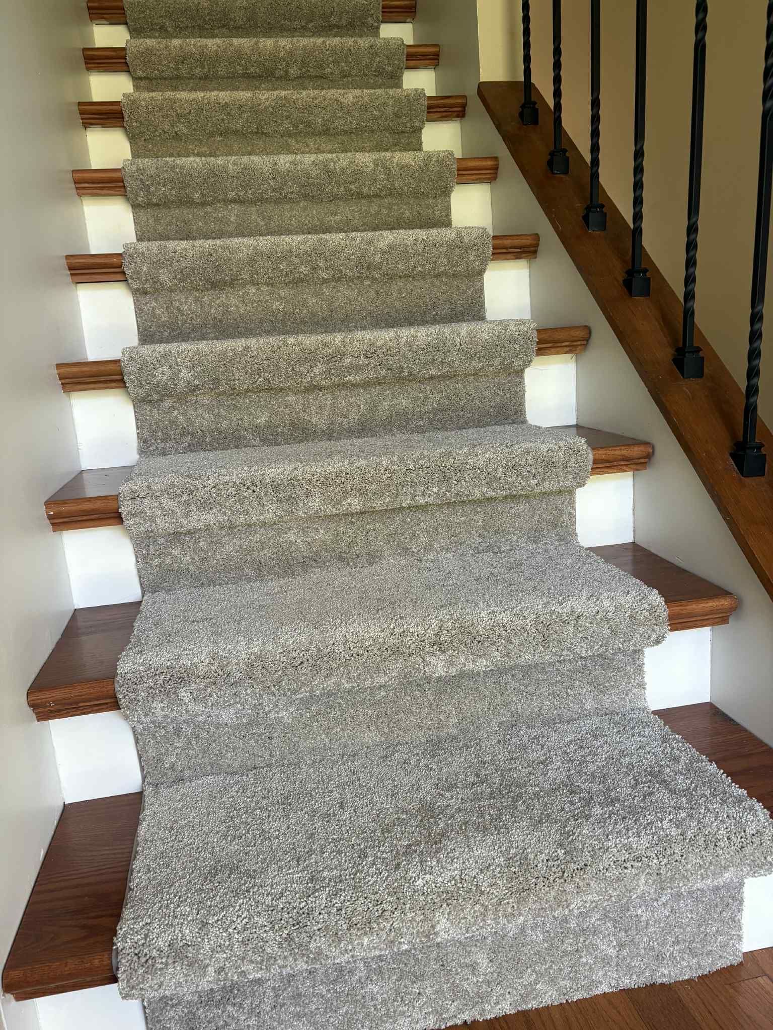 Staircase with carpet runner, brown wood steps, white risers, black iron railing.