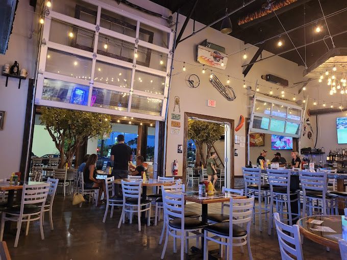 Restaurant interior with tables and chairs, open garage doors, string lights, and patrons.