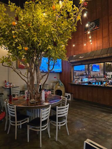 Restaurant interior with a large tree centerpiece, bar, tables, and chairs.