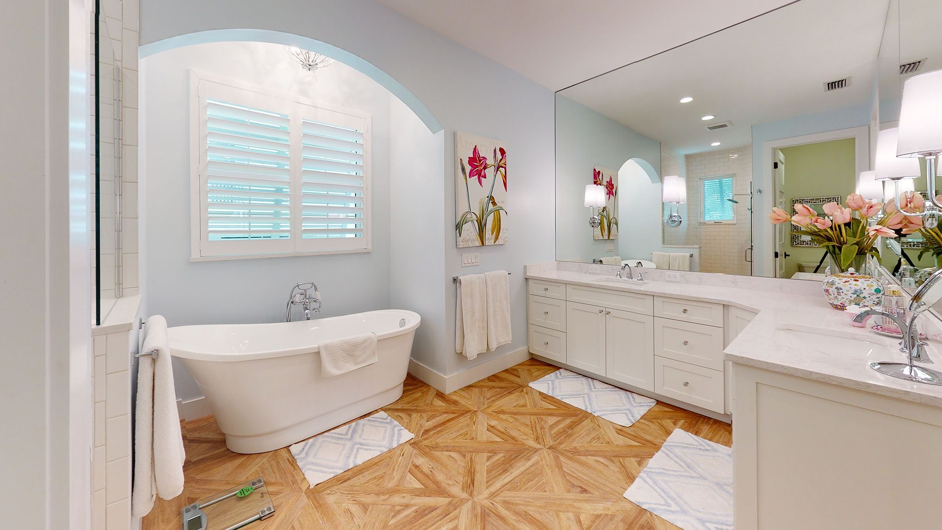 Bathroom with a claw-foot tub, large mirror, white cabinets, and a wood-patterned floor. Soft blue walls.