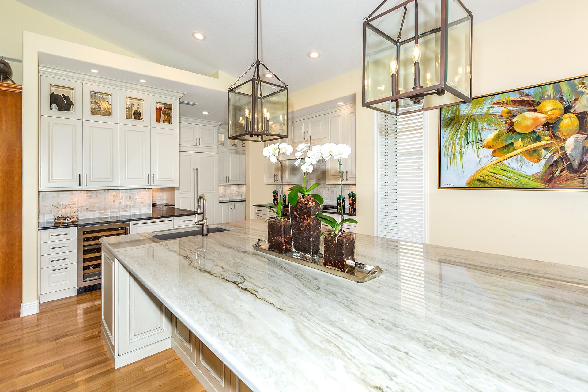 Modern white kitchen with a large marble island, two lantern lights, and art.