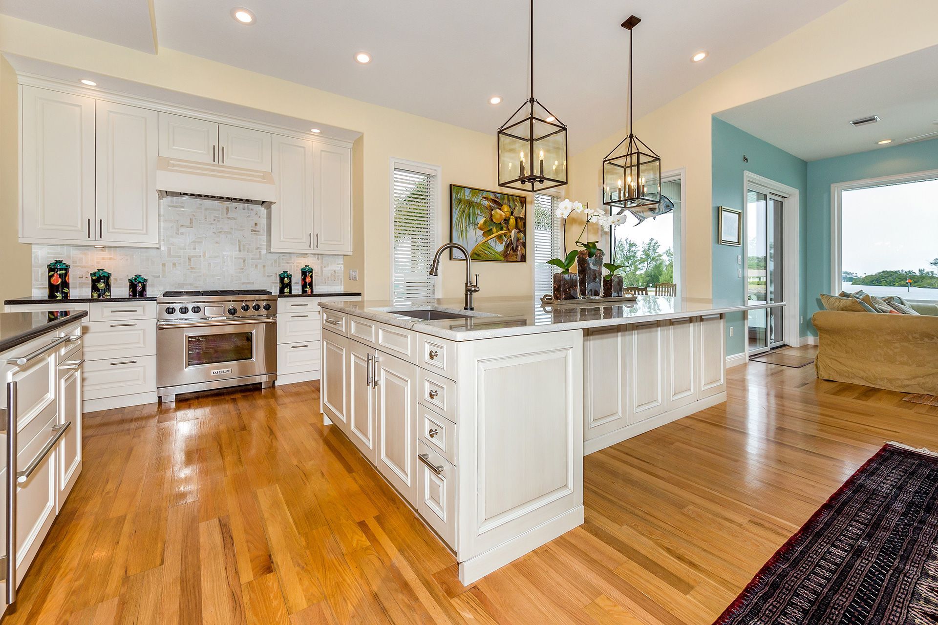 Bright, white kitchen with an island, wood floors, stainless steel appliances, and two hanging lanterns.