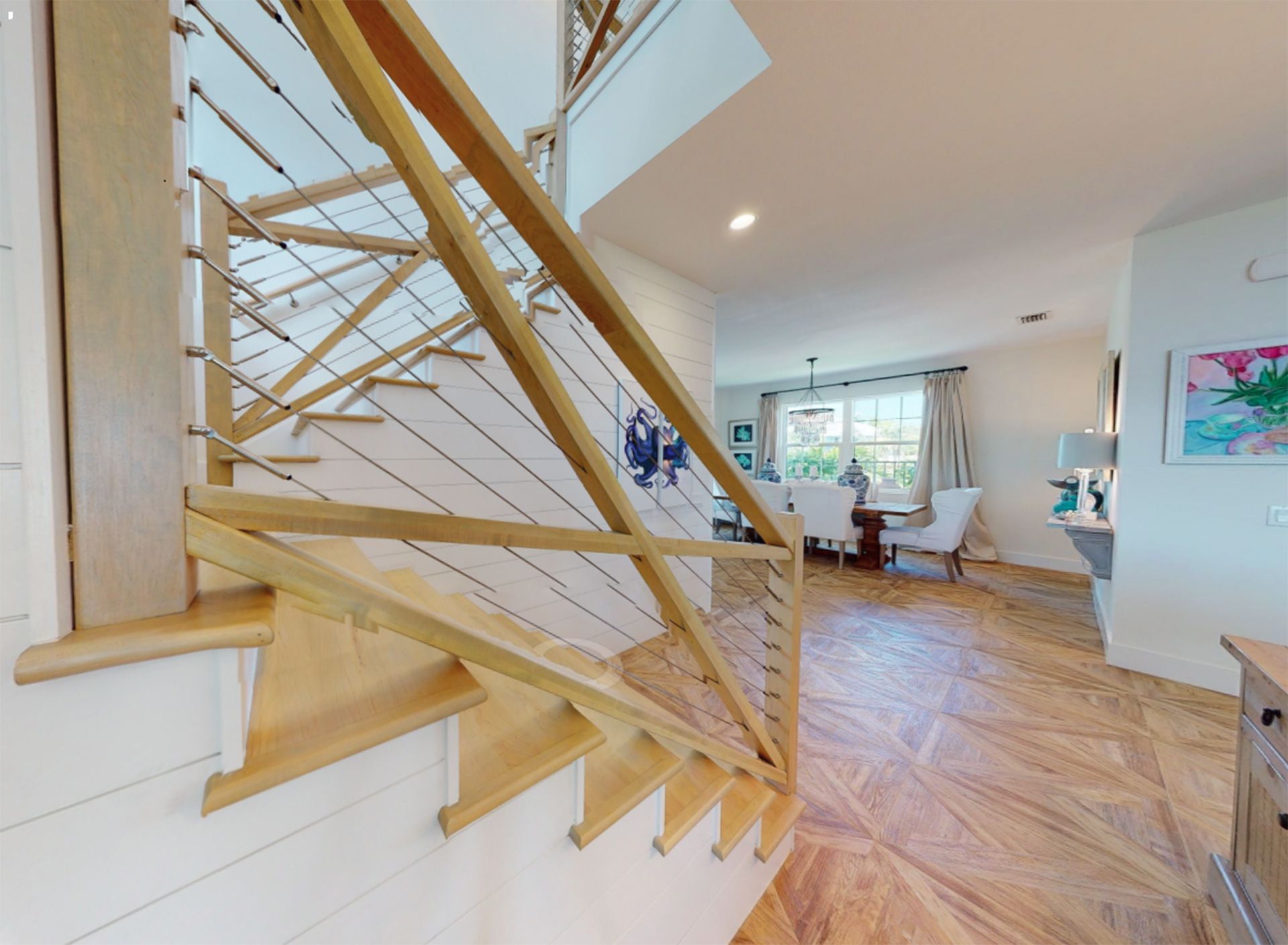 Staircase with wooden steps and railing, leading up. An open floor plan is visible in the background with a dining table.
