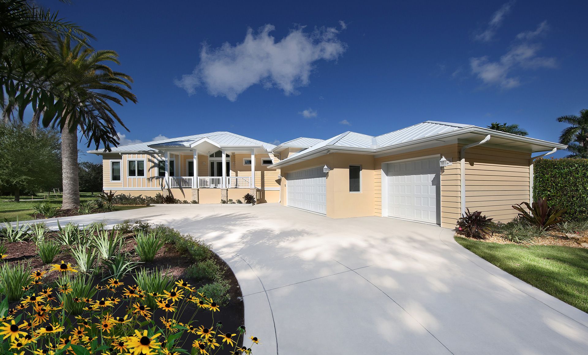 Light beige Florida-style home with white trim, arched driveway, and lush landscaping on a sunny day.
