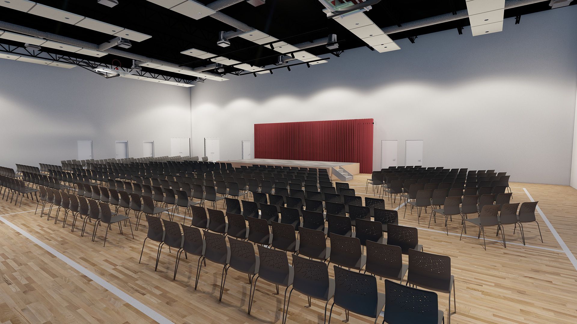 Rows of black chairs face a stage with red curtains in a large hall with wood flooring.