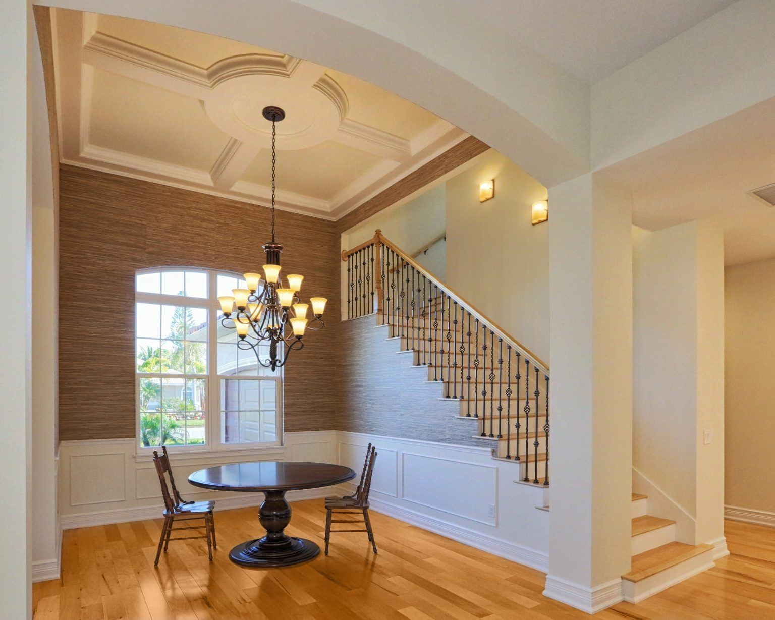 Formal dining room with dark round table, chairs, chandelier, and staircase.