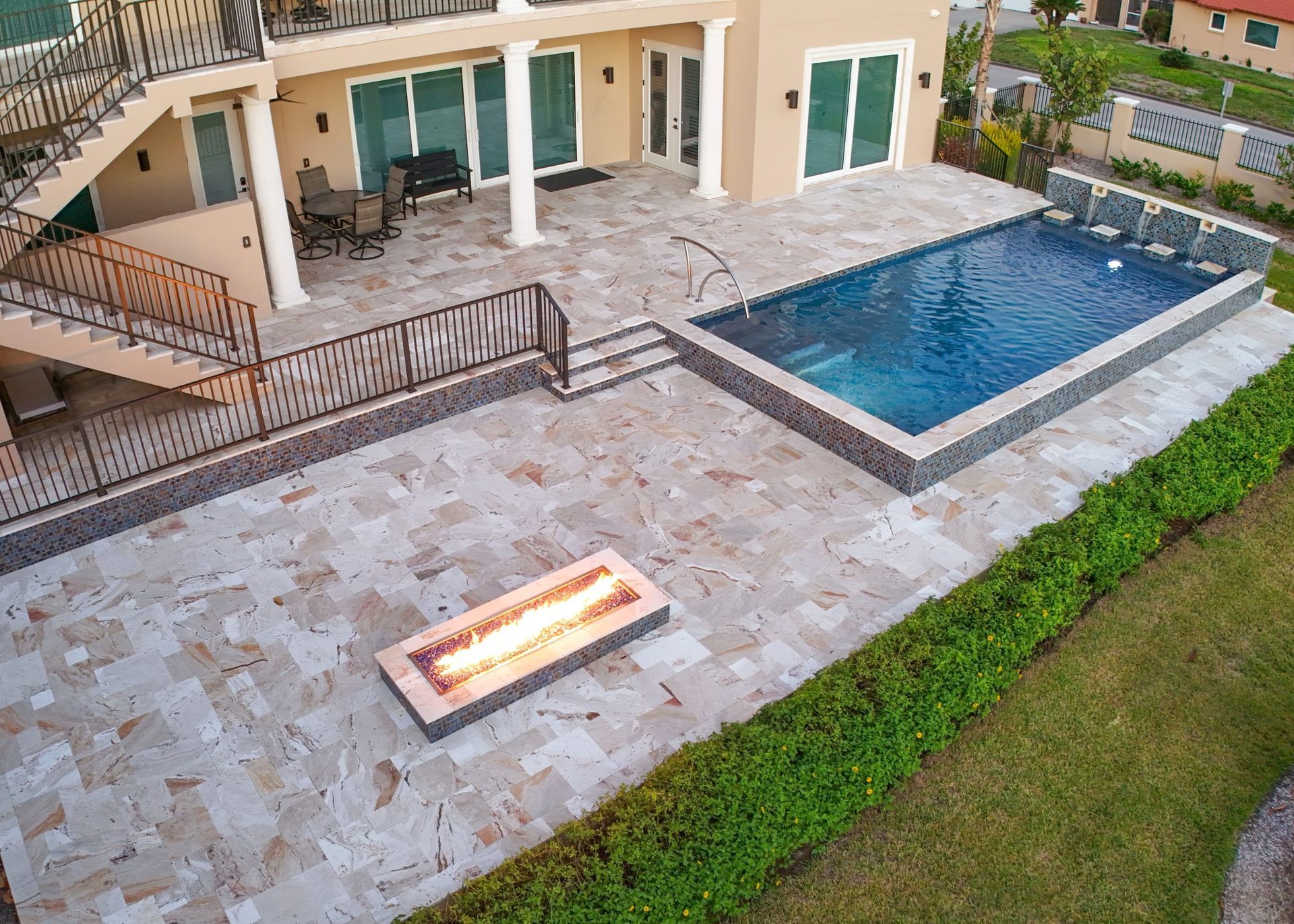Backyard patio with rectangular pool, fire pit, and stairs leading to second-story balcony.