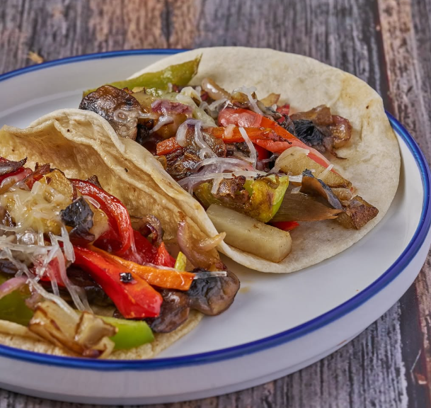 Two vegetarian fajitas on a white plate with blue rim, featuring grilled vegetables and cheese.