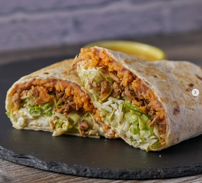 Burrito cut in half, filled with rice, lettuce, meat, and sauce on a black plate.