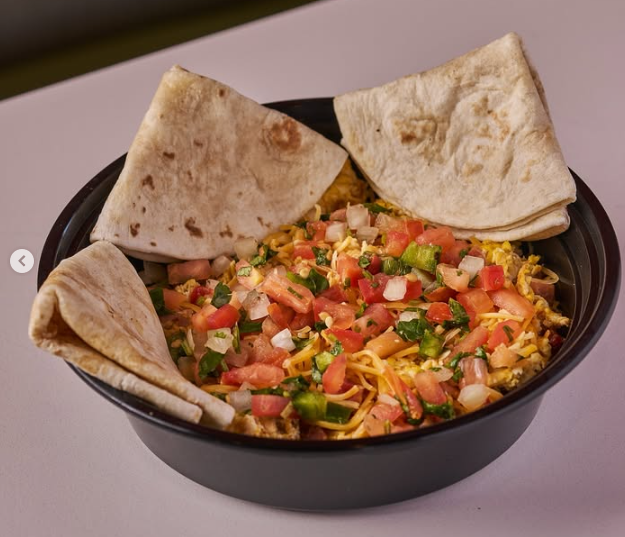 Breakfast bowl with scrambled eggs, pico de gallo, and tortillas in a black bowl.