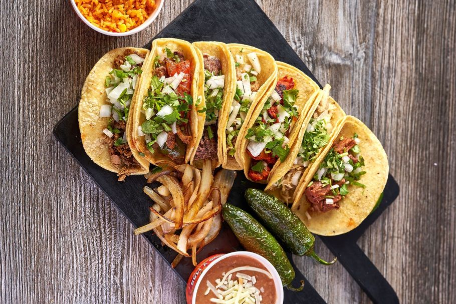 Tacos with toppings, onion rings, jalapenos, and salsa on a wooden surface.