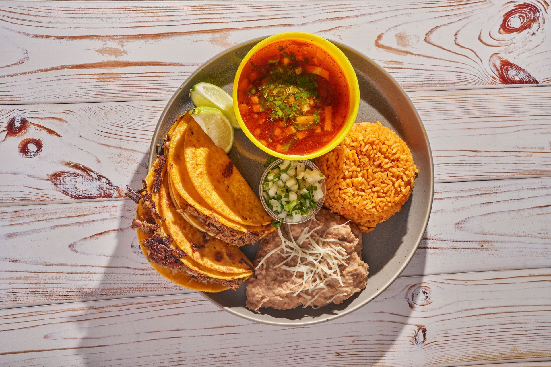 Mexican meal on a plate: tacos, soup, rice, beans, lime, and salsa.