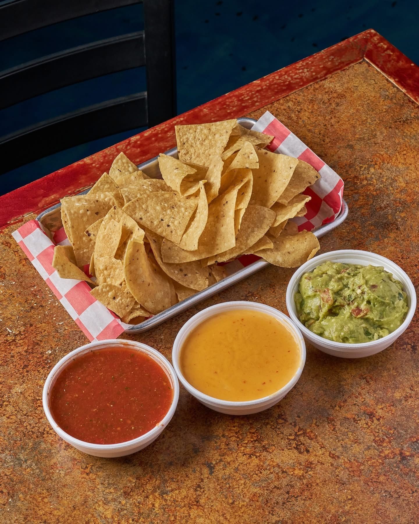 Chips with salsa, queso, and guacamole dips on a table.