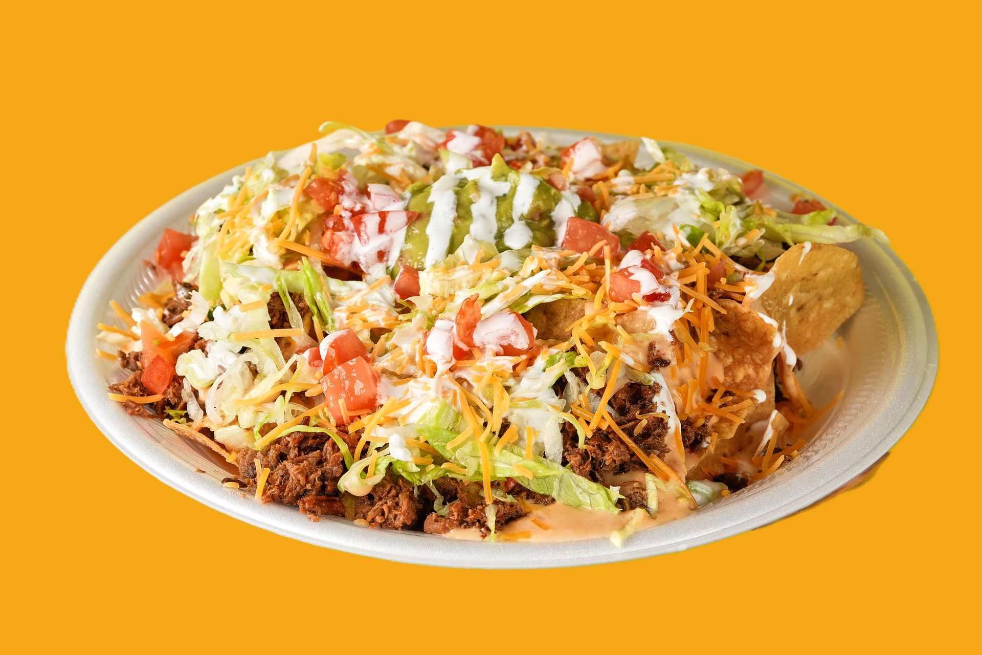 Loaded nachos with beef, cheese, lettuce, and toppings on a white plate, orange background.
