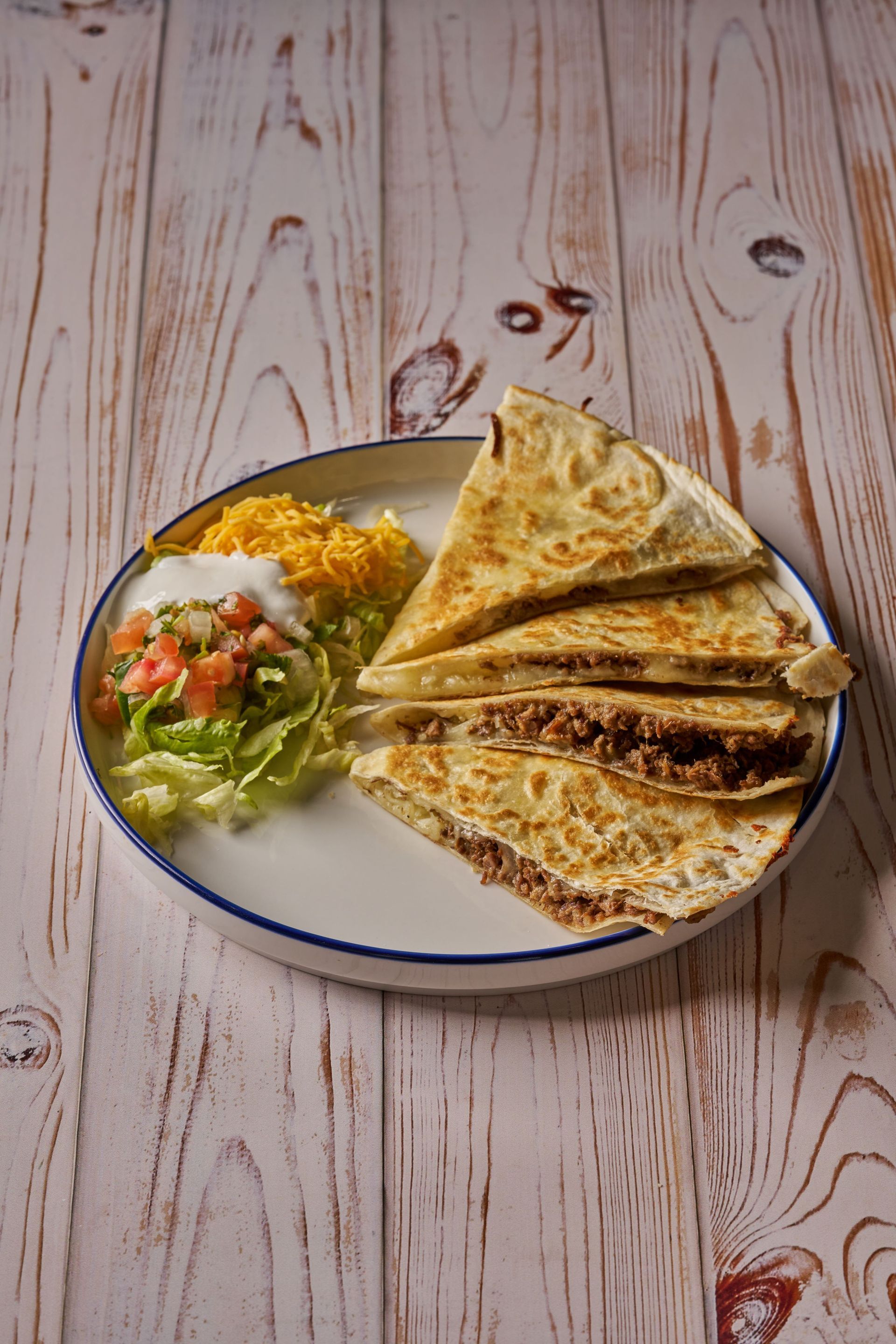 Quesadillas with sides of lettuce, salsa, shredded cheese, and sour cream on a plate.