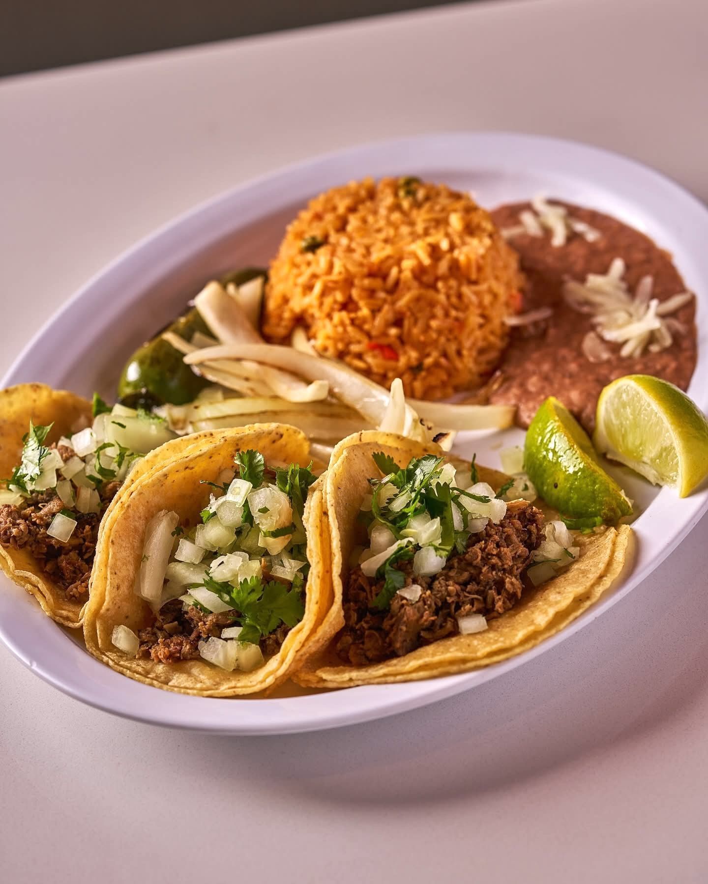 Plate of tacos with rice and beans, garnished with lime and onions.