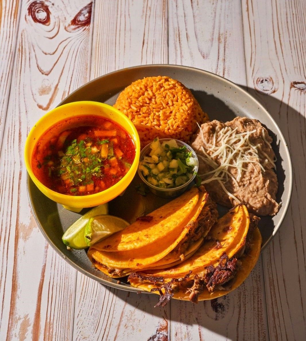 Plate with tacos, refried beans, red rice, soup, and salsa.