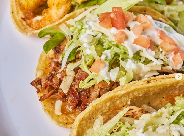 Close-up of three tacos: one with pulled pork, toppings, and one with shrimp.