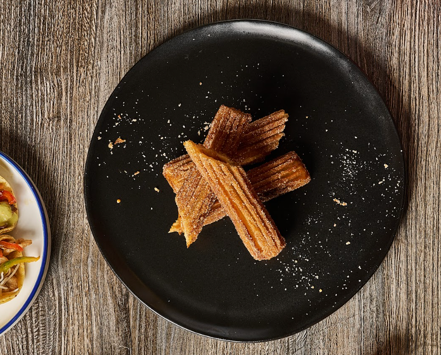 Churros on a black plate sprinkled with sugar, placed on a wood table.