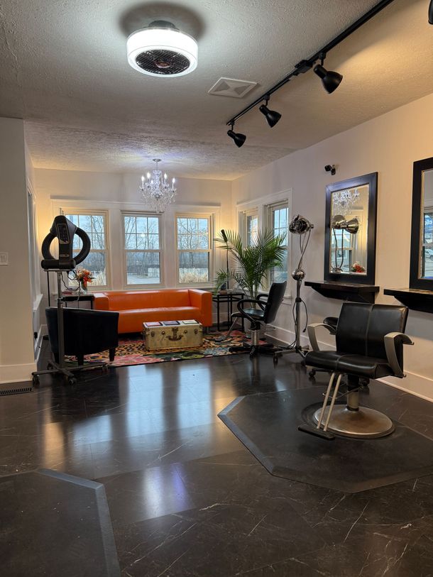 Modern salon with orange couch, black chairs, mirrors, and large windows under track lighting