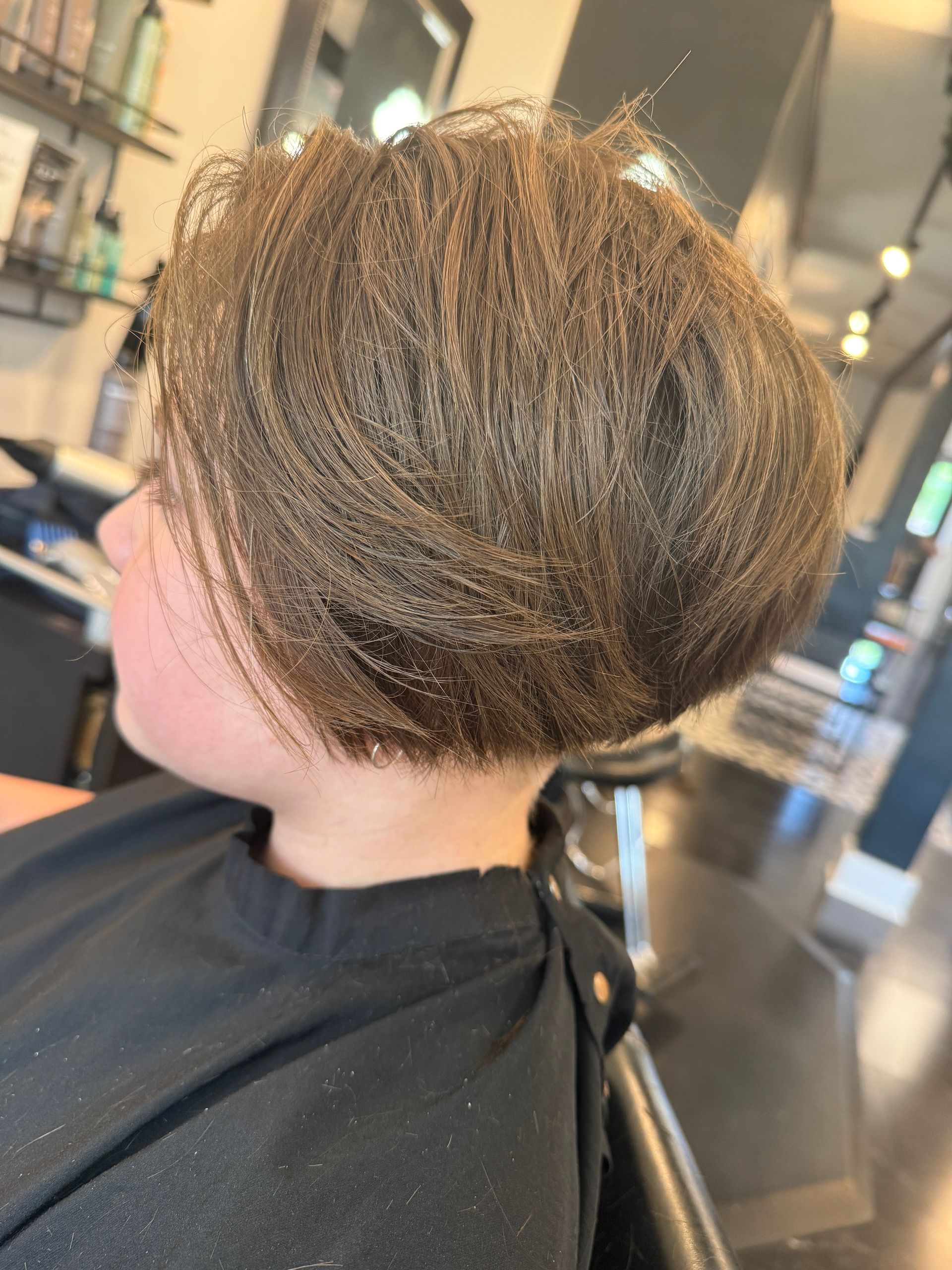 Short layered brown haircut viewed from the side in a salon chair
