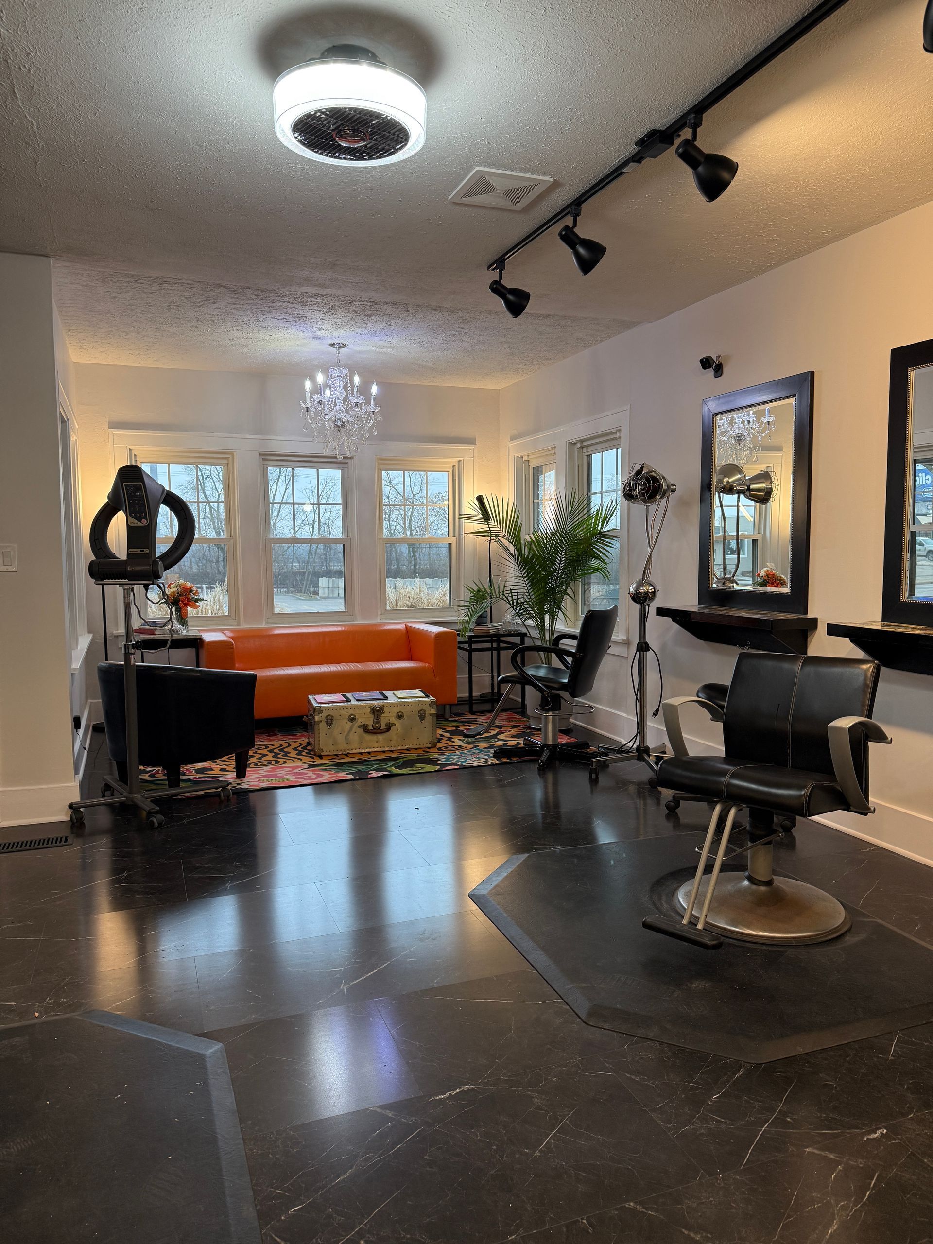 Modern salon with black chairs, orange couch, large windows, and track lighting